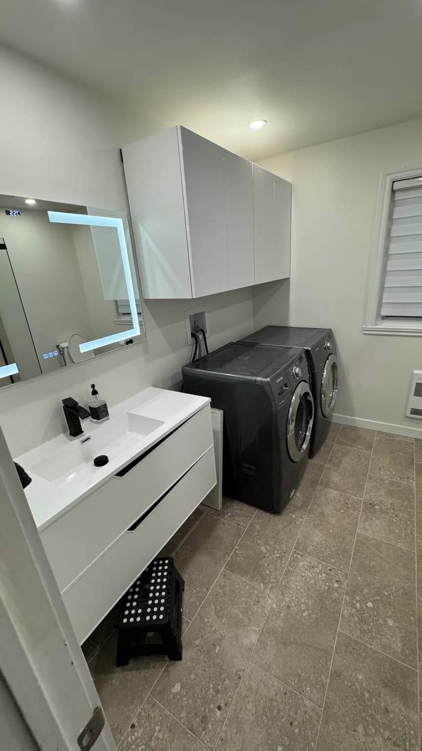 Renovated bathroom and laundry room in Pierrefonds-Roxboro with glass shower, wall-mounted vanity and laundry area.