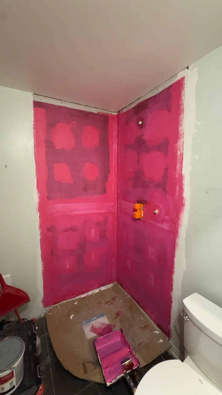 Corner shower after application of the pink waterproofing membrane.